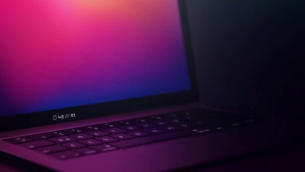 Nyitott laptop félhomályban, a képernyőn rózsaszín-lila színátmenet